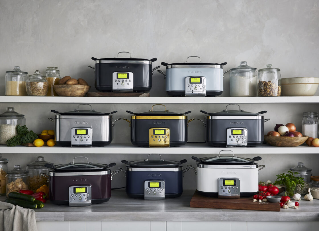 Image of 7 slow cookware in a kitchen along shelves in different colors including, blue, slate, purple, white, baby blue and stainless steel.