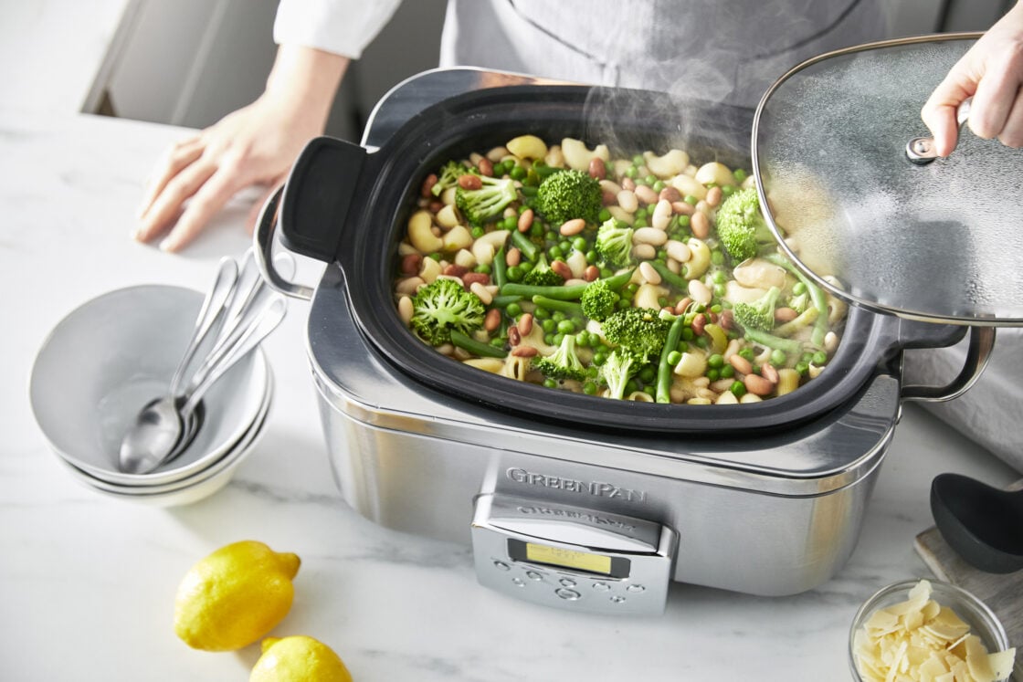image of chef standing behind the greenpan slow cooker filled with a grew stew of broccoli beans and more.