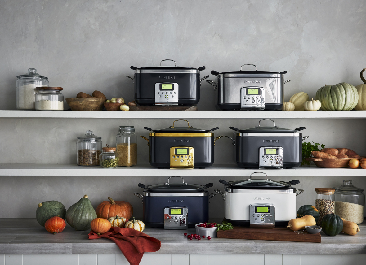 Image of 6 GreenPan Slow Cookers in various colors/finishes/ and lines. Lined up on the counter and two shelves above. The image is also styled with squash and pumpkins, glass canisters of pantry staples, and a wood cutting board.