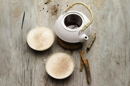 Image of an overhead view of a kettle and two clear glass mugs with a hot toddy recipe with tea and bourbon on a wood table.