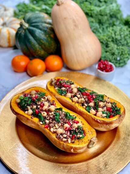 vegetarian stuffed butternut squash on a gold charger with clementines, squash, pomegranate arils, and kale in the backgroud.