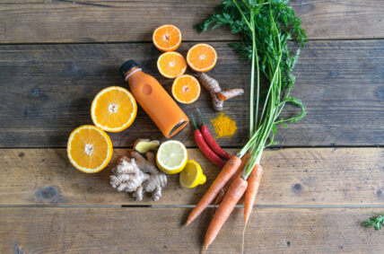 image of orange juice laid out with the ingredients to make it: carros, chili peppers, oranges, ginger, lemon, and turmeric showing juice cleanse via Organic Authority.