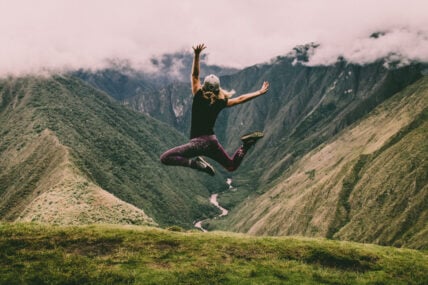 woman leaping high over a beautiful view of the valley - ways to keep your mitochondria strong