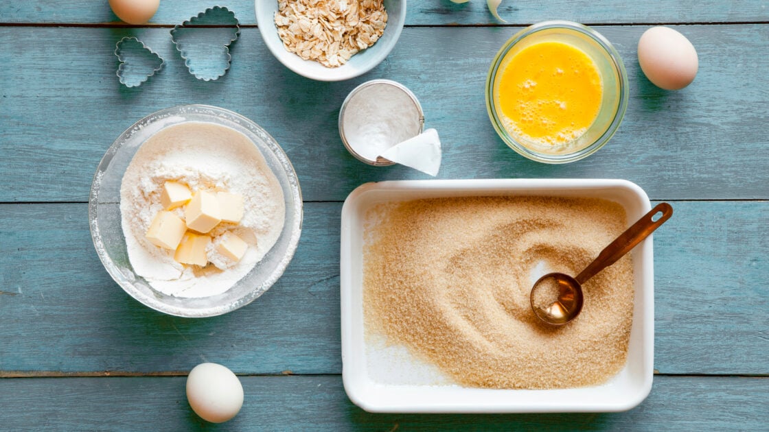 Find safe non-toxic bakeware for your kitchen via Organic Authority's Guide. Image of baking ingredients on a blue board including butter, flour, eggs, sugar, baking powder.