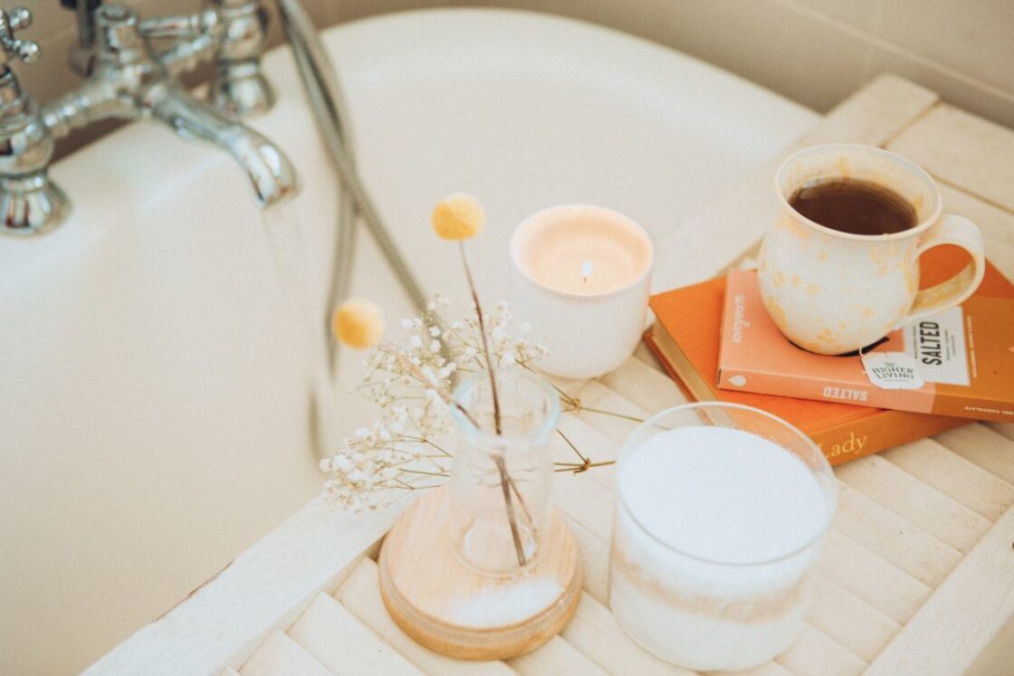 Image of non-toxic natural candle burning over the bathtub with a cup of tea and dried flowers and books. Relaxing scene