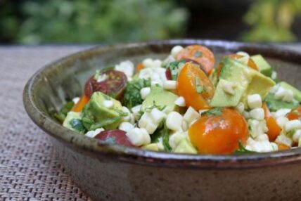 Image of a dark bowl of fresh corn, avocados, and tomatoes in a healthy avocado recipe