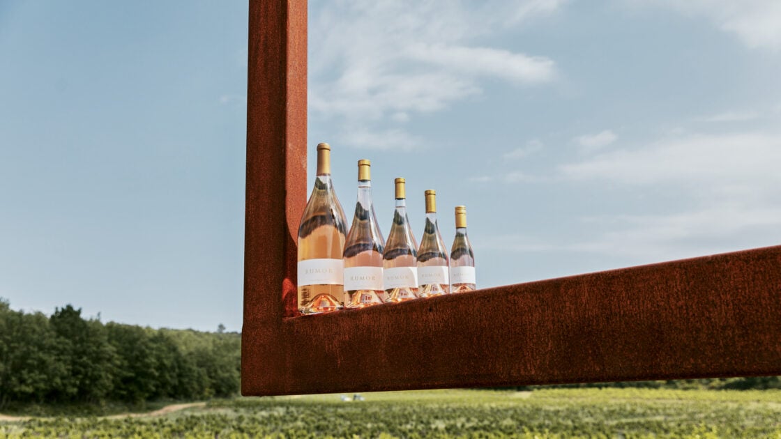 image of five bottles or Rumor organic wine outside against a blue sky background.