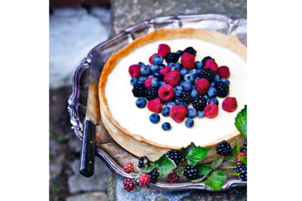 Image of a creamy white panna cotta pie topped with fresh berries and served on a silver platter with a sprig of fresh blackberries alongside.