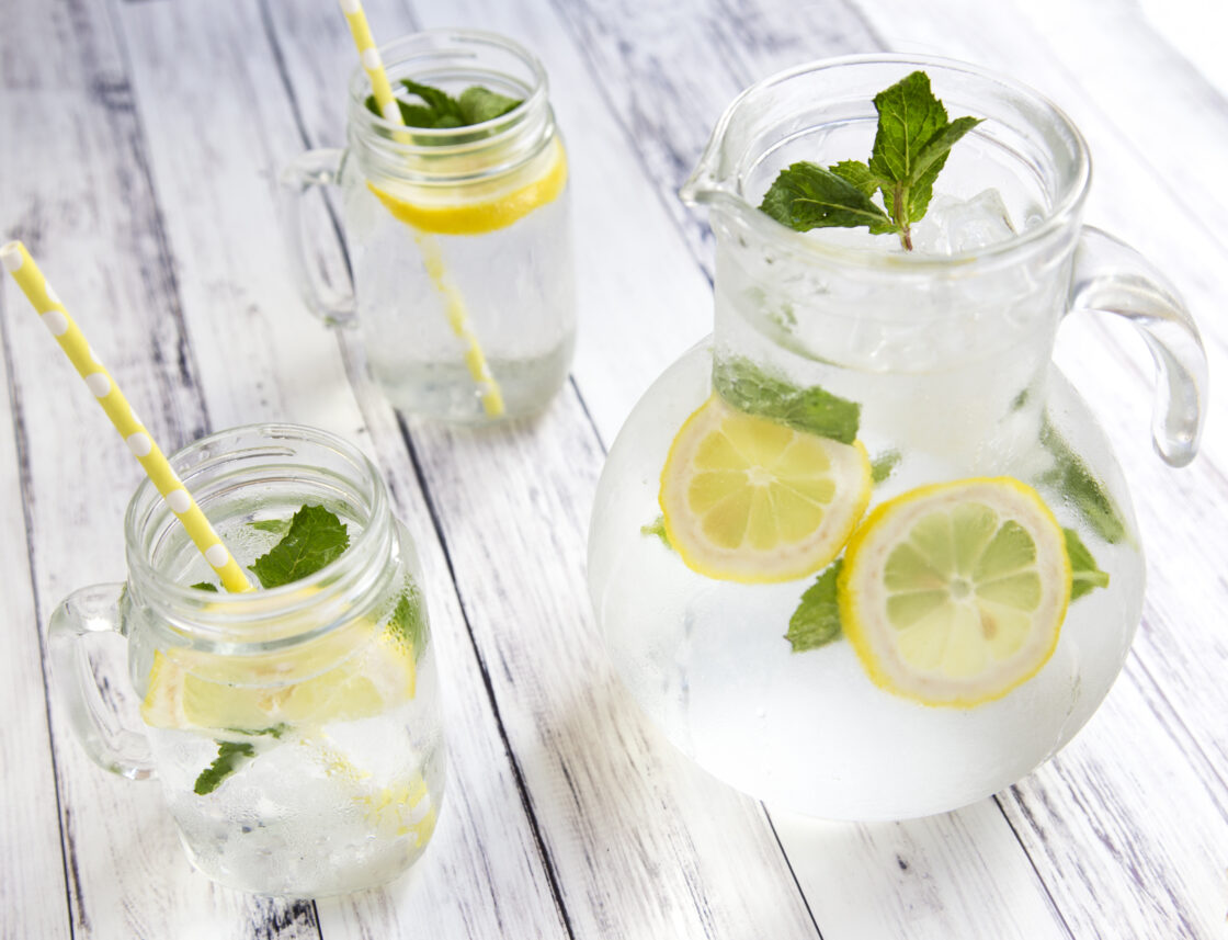 Image of a pitcher of vodka cocktail with sliced lemons and mint, with glasses filled with the same organic sustainable drink for ta boozy brunch.
