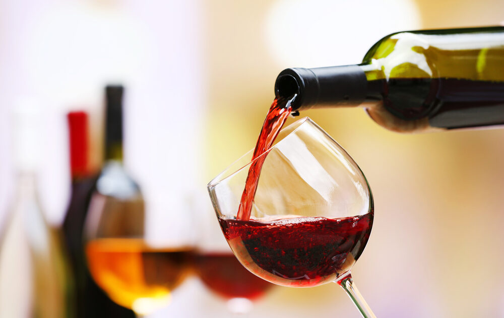 Image of red wine from Stag's Leap Wine Cellars being poured into a red wine glass with blurred out wine bottles and glasses in the background.