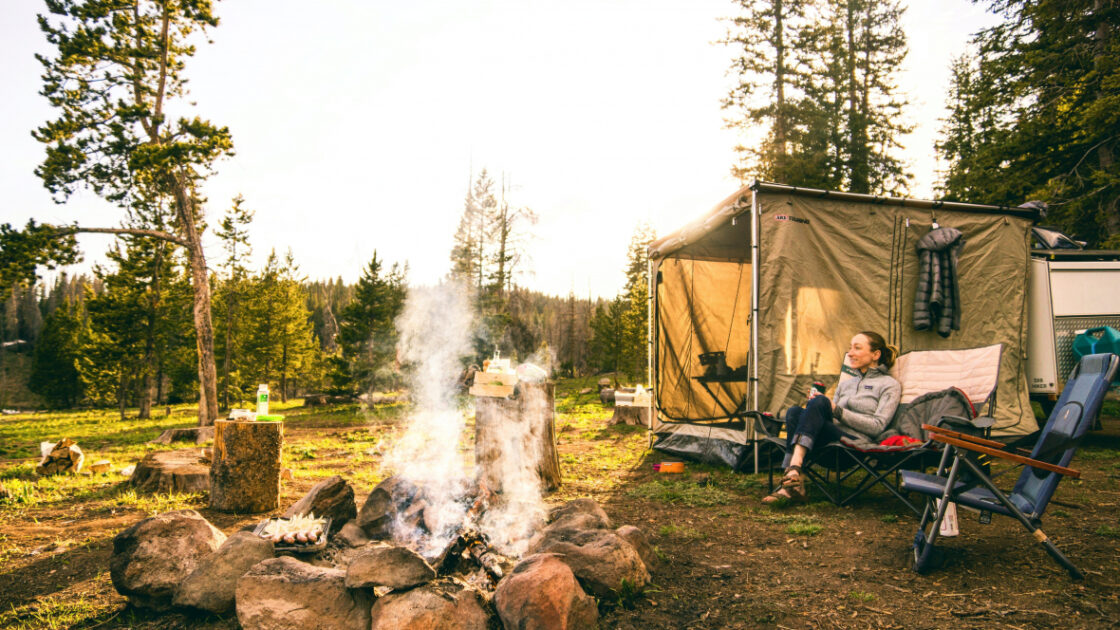woman sitting next to tent and campfire