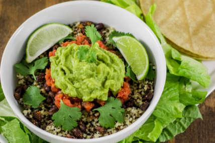 Image of Burrito Bowl with Spiced Black Beans and Quinoa Recipe served in a white bowl on a white platter with lettuce and corn tortillas on a wood table.