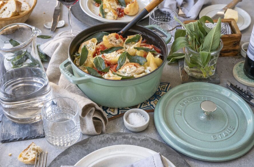 Image of a sage green Staub cast iron cocotte full of large stuffed pasta shells.
