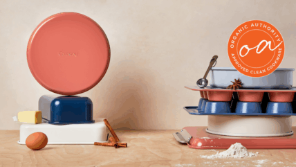 Image of the set covered in this Caraway Bakeware review, shown in mixed colors (perracotta, navy, and white) in two stacks with a single brown egg, half stick of butter, and sprinkle of flour on the wooden work surface.