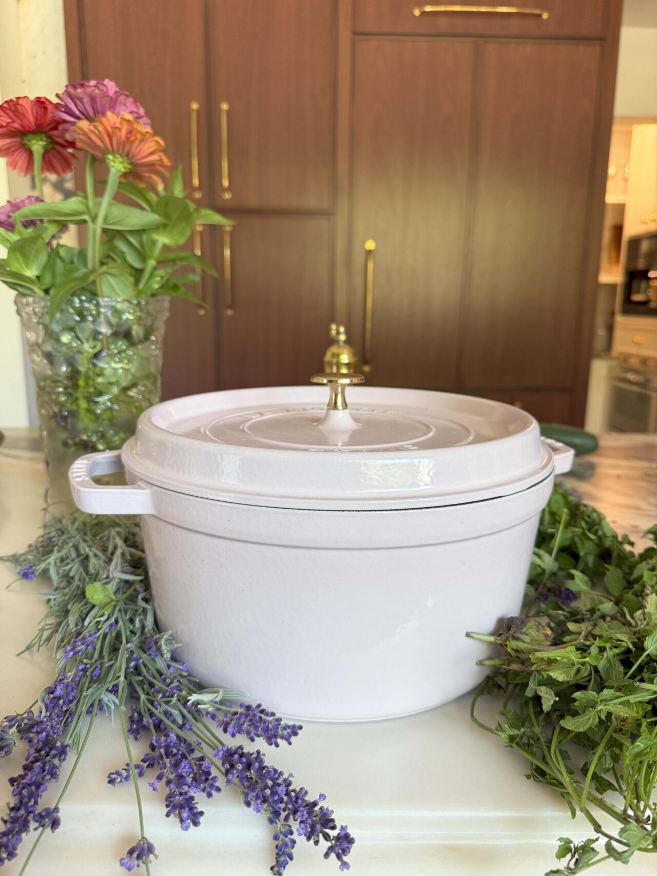 Image of Laura Klein's Staub Coq au Vin Dutch Oven in white, shown on a marble countertop next to colorful flowers.