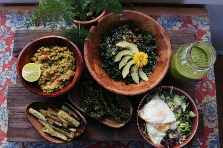 overhead view of Kitchari, made from soaked mung beans, rice, and warming spices in an earthen bowl surrounded by other bowls of wholesome food and green juice