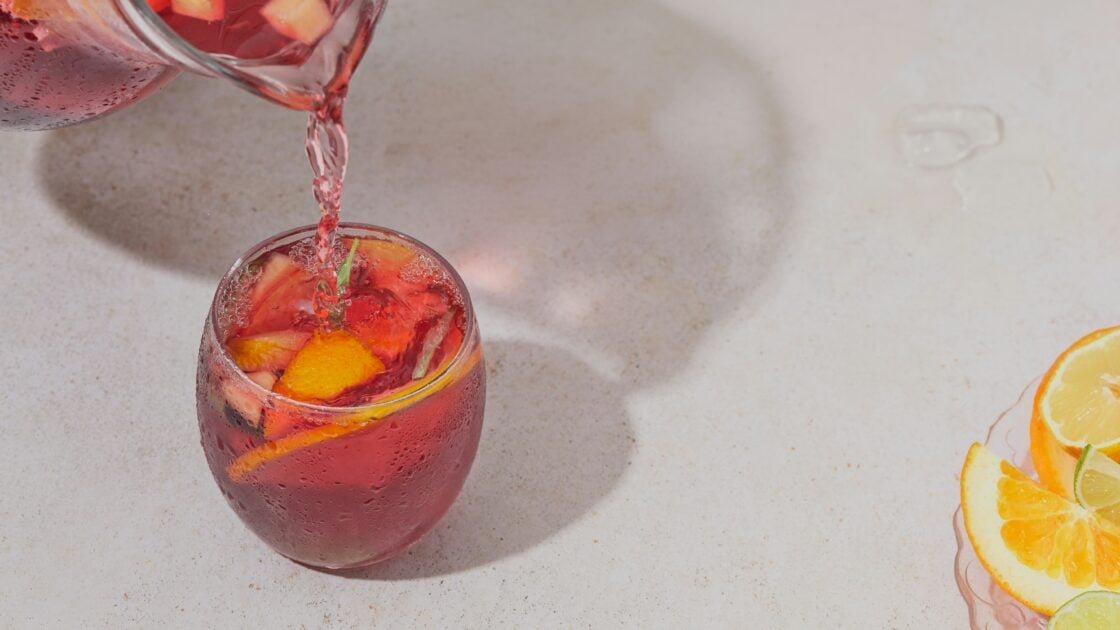 image of a pink sangria drink being poured into a glass with fruit garnish