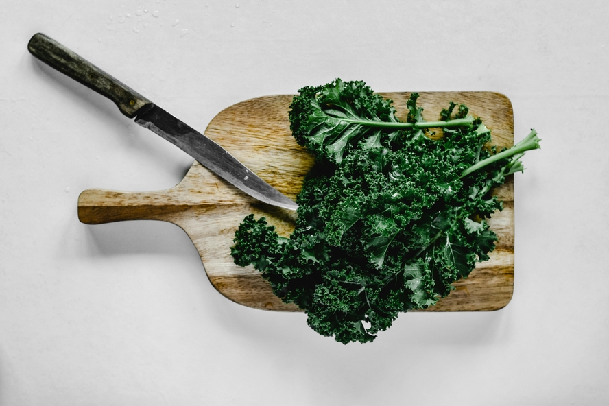 Image of a leafy bunch of kale on a wooden cutting board next to a knife.