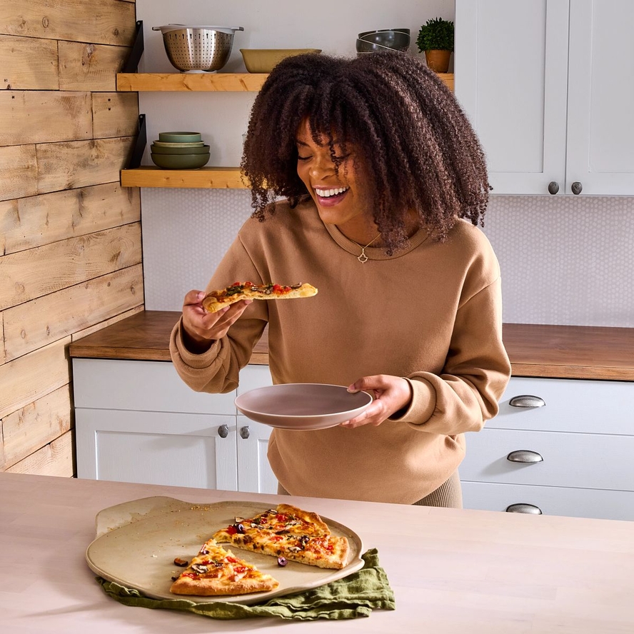 Image of a woman taking a slice of pizza off Pampered Chef's pizza stone.