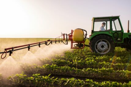 Can pesticides cause cancer? New research suggests that it can. Image of a farmer in a tractor spraying pesticides over a field.