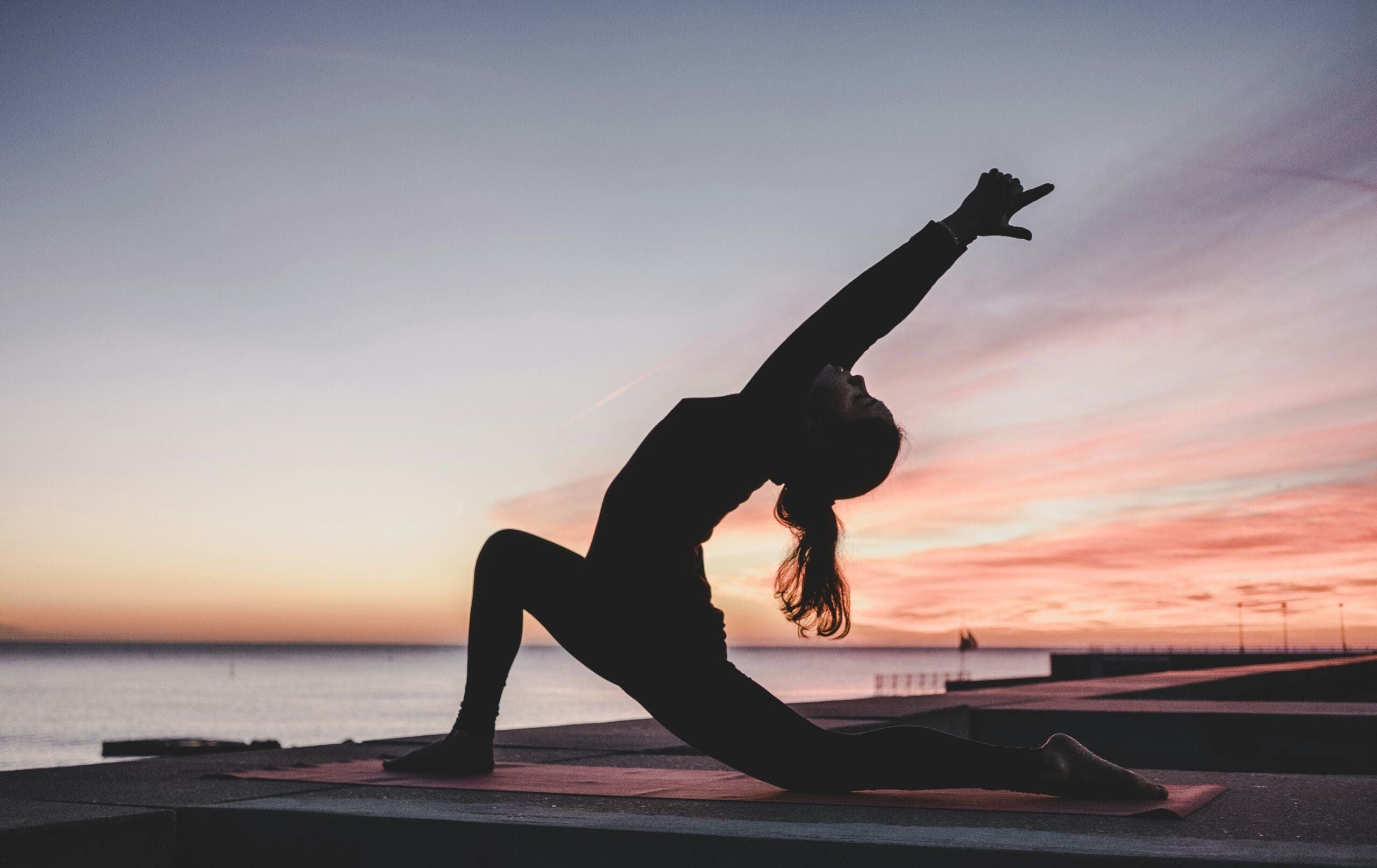 Silhouette of a person doing a backbend yoga pose on a beach at sunset
