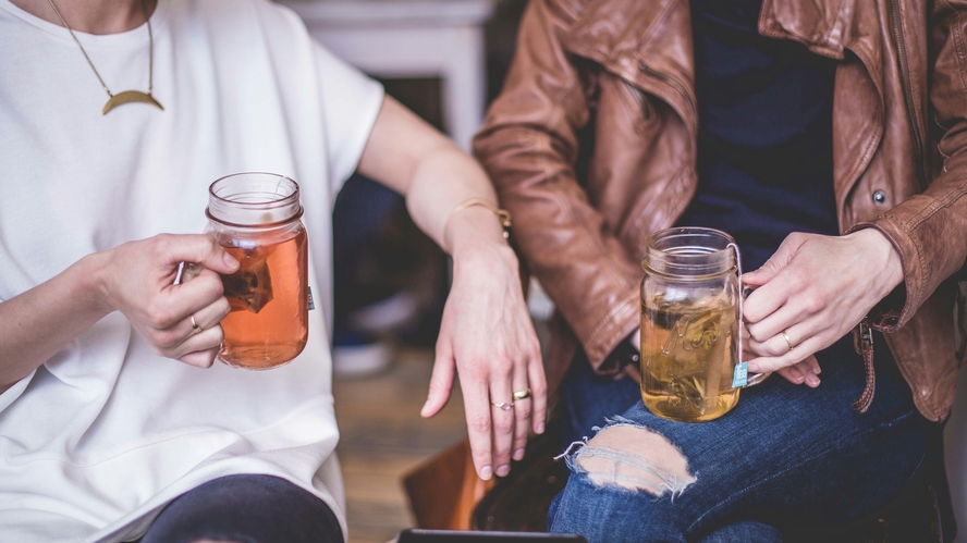 Image of two women sitting down and each drinking a cup of tea from a mason jar.