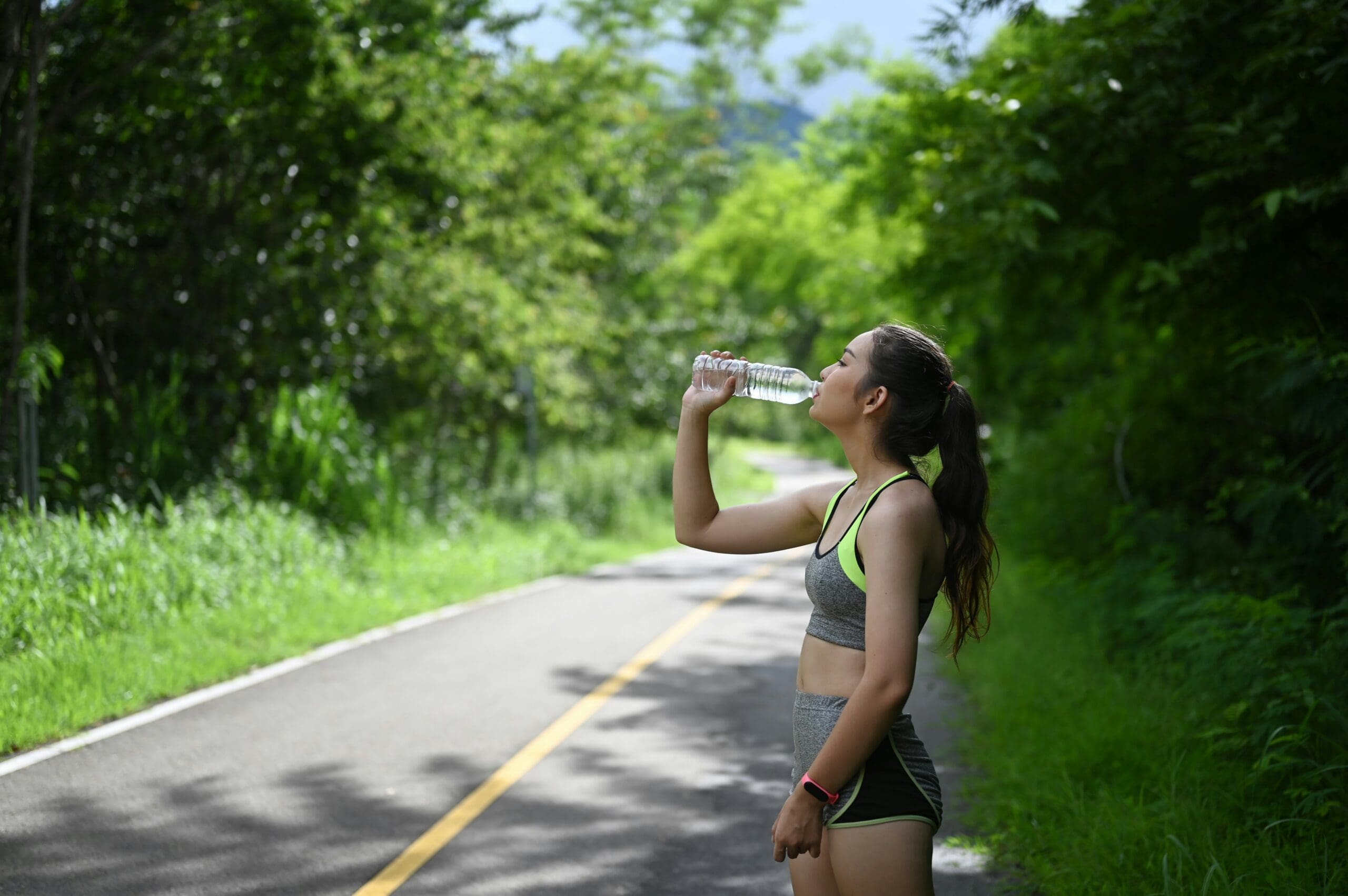 Image of woman drinking water on a road dressed in athletic gear. Drinking water is a good way to curb sugar cravings and avoid sugar hangovers.