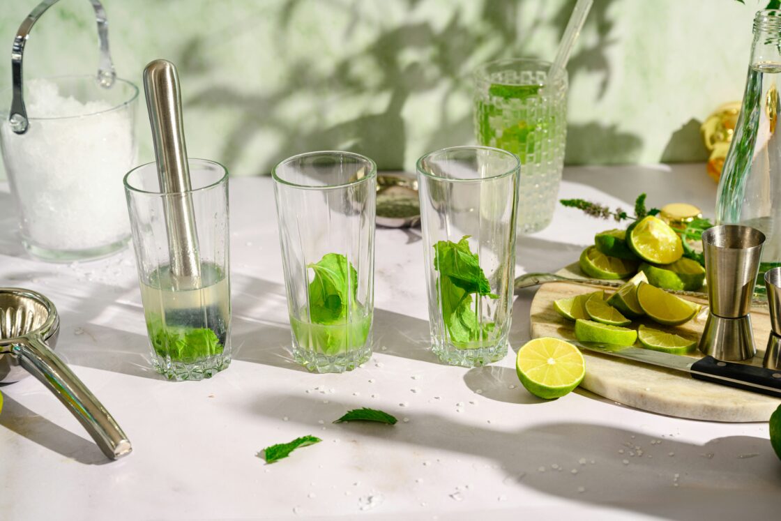 Image of green juice drinks being prepared in clear glasses with muddled mint