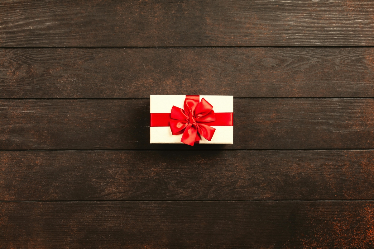 Image of a small white gift box with a red ribbon on a wooden tabletop.