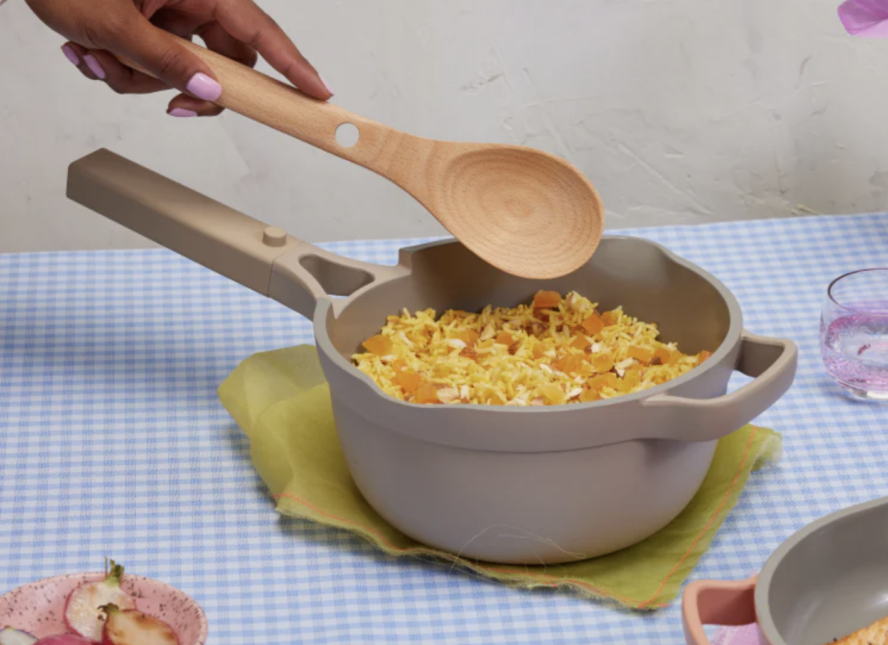 Image of the Our Place Mini Perfect Pot, filled with a pilaf rice and a hand reaching to stir it with the included Beechwood Nesting Spoon.
