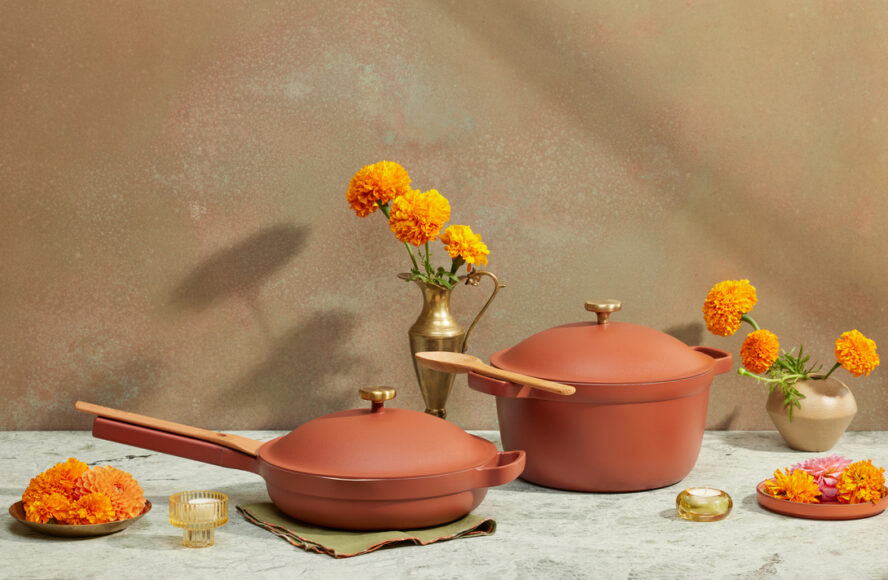 Image of the Our Place Always Pan and Perfect Pot, displayed on a table with beautiful orange marigolds surrounding them.