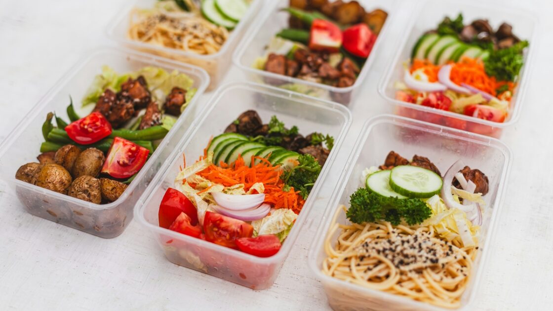 Image of six plastic food storage containers filled with prepped meals of noodles, vegetables, and proteins.