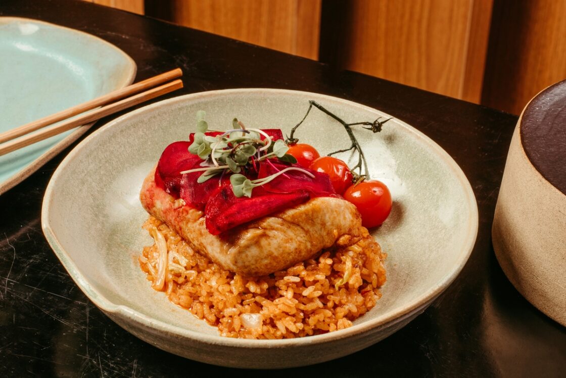 Image of a baked fish filet on a bed of rice, topped with fresh and steamed vegetables.