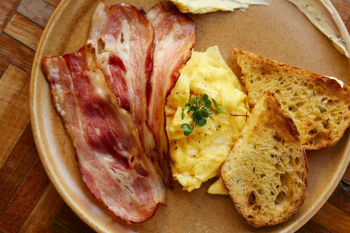 Image of a breakfast plate with two slices of toast, scrambled eggs, and several slices of bacon.