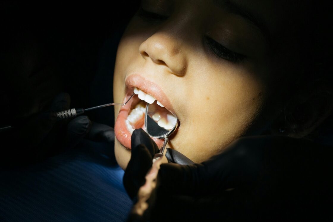 Image of a child sitting in a dentist's chair, with dental tools in their mouth and a light illuminating their face.