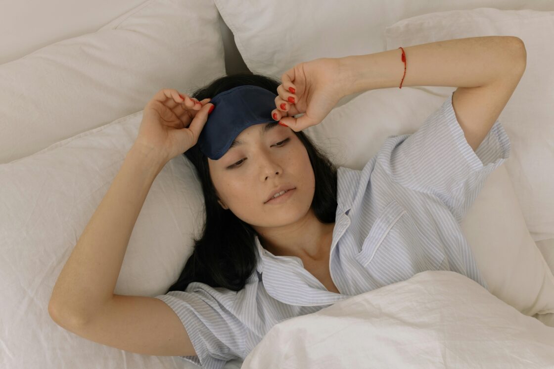 Image of a woman in bed wearing pajamas with an eye mask on her forehead as she prepares to sleep.