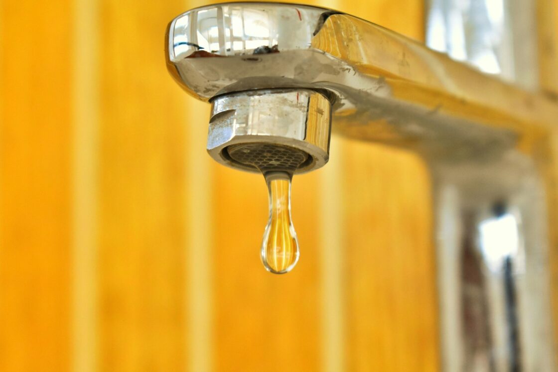 Close-up image of a silver water faucet with a drop of water poised to fall.