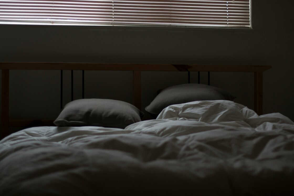 Image of a darkened bedroom with very little light illuminating a comfortable bed.