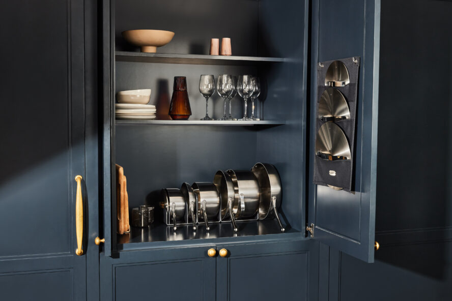 Image of Caraway cookware in stainless steel put away beautifully in a dark blue cabinet.