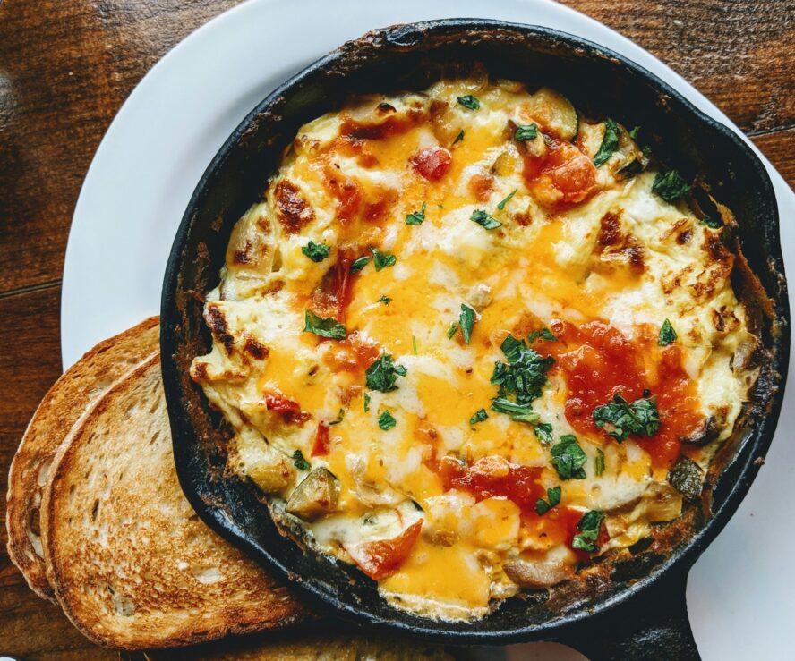 Image of a black cast iron pan with a cheesy egg and tomato mixture and a couple slices of sourdough toast.