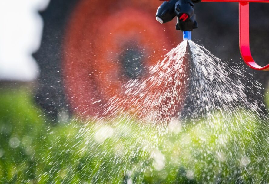 Image of a tractor spraying pesticides over a field of crops which may be included on the Dirty Dozen list.