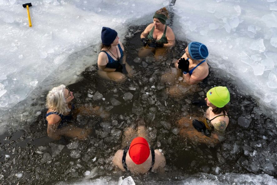 Image of a group of six woman taking a cold plunge together in an ice-covered lake.