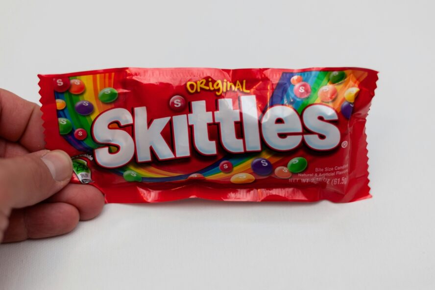 Image of a hand holding up a packet of Skittles against a white background — a product that will no longer be on the list of foods with titanium dioxide.