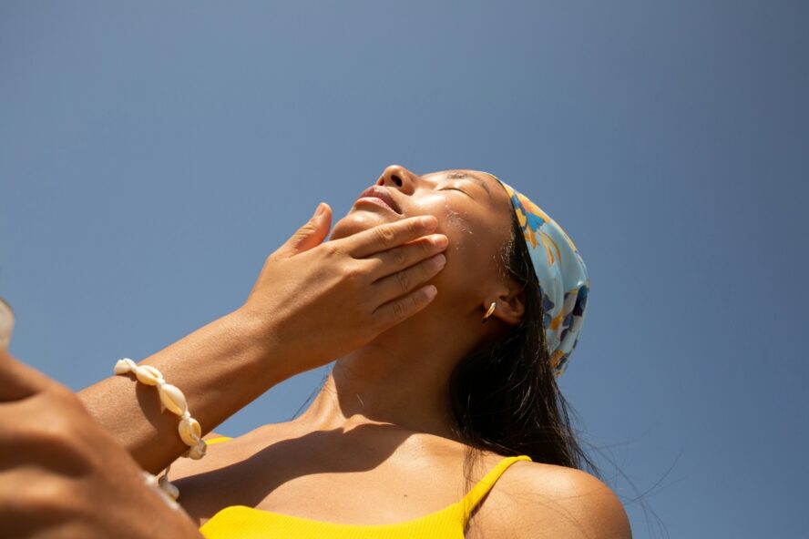 Image of a young woman applying sunscreen on her face, which often includes titanium dioxide.