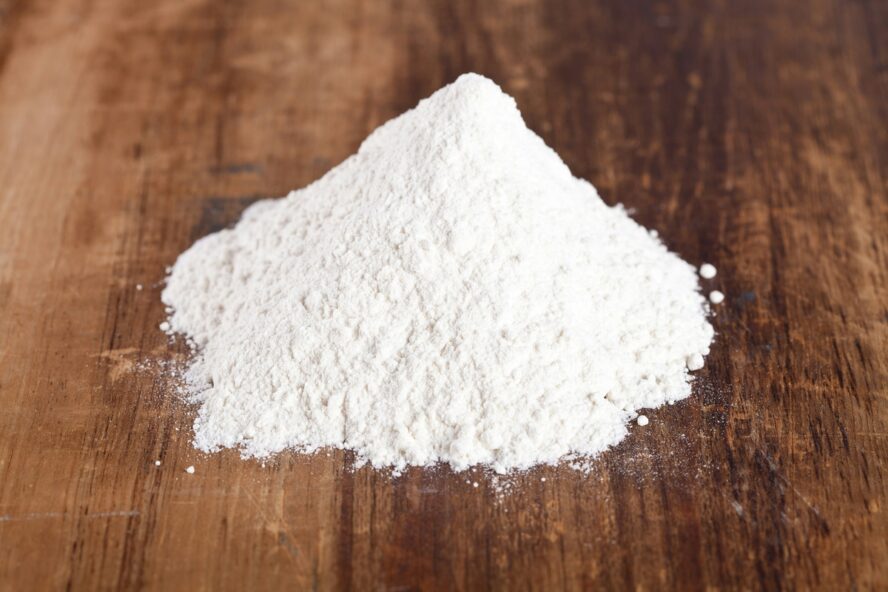 Image of a pile of white powdered calcium phosphate on a wooden table surface.