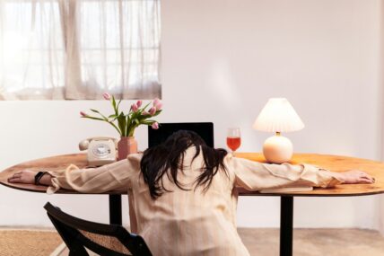 Image of a woman with her arms splayed on a desk in front of her laptop, with her head resting on the table.