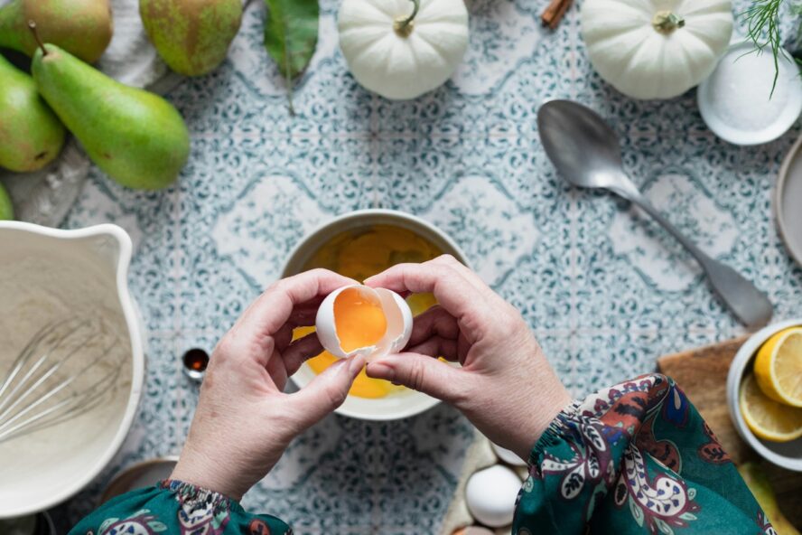 Image of a woman's hands breaking open an egg and separating the yolk from the white over a bowl for baking.