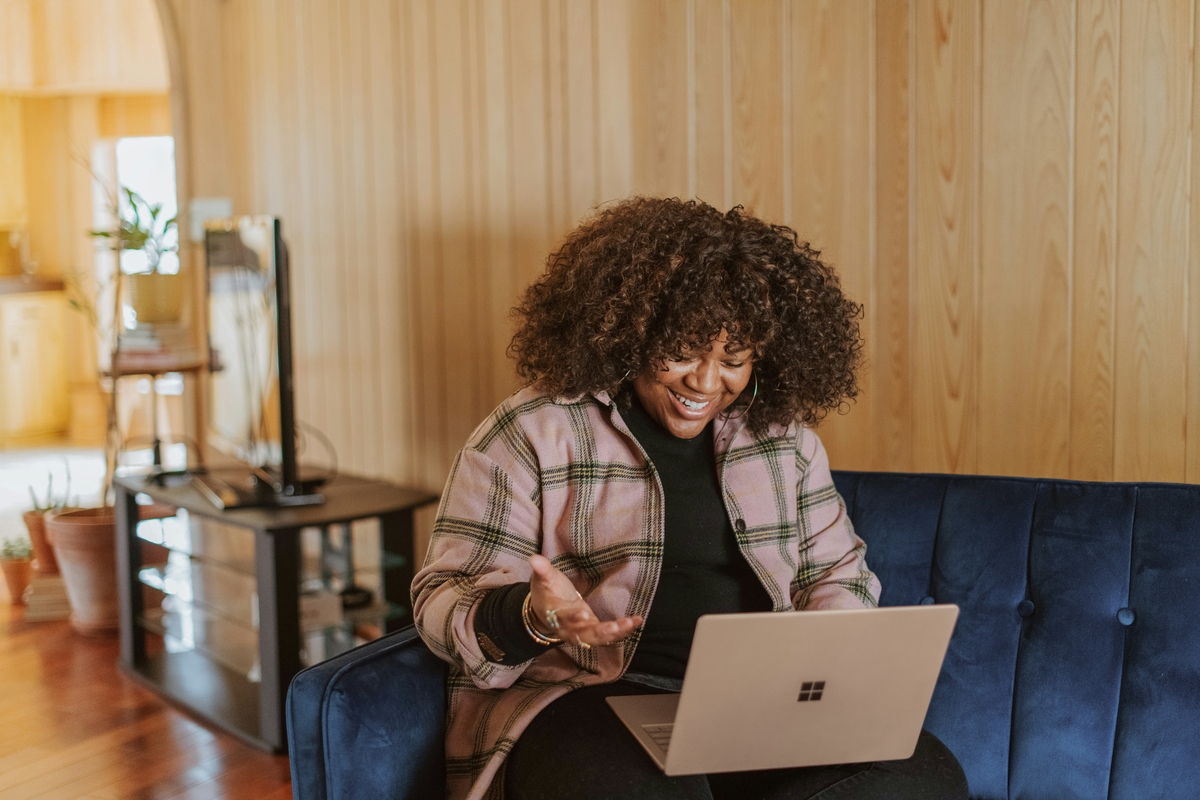 Image of a woman sitting on a couch smiling at her laptop.