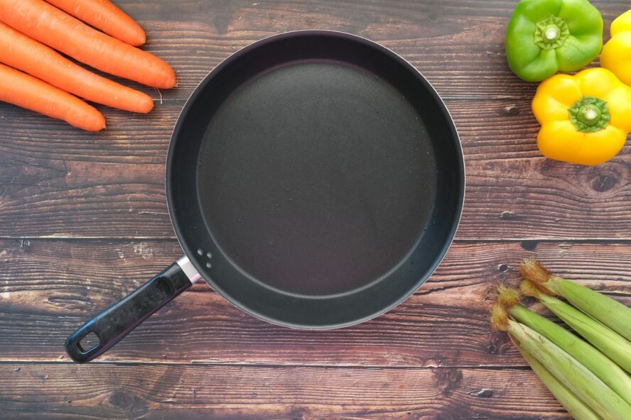 Image of a traditional nonstick pan on a wooden table, surrounded by fresh vegetables.