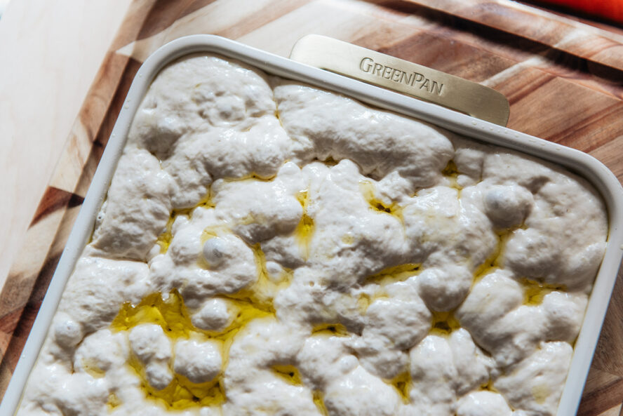 Image of a sheet pan of focaccia dough, stretched and dimpled.